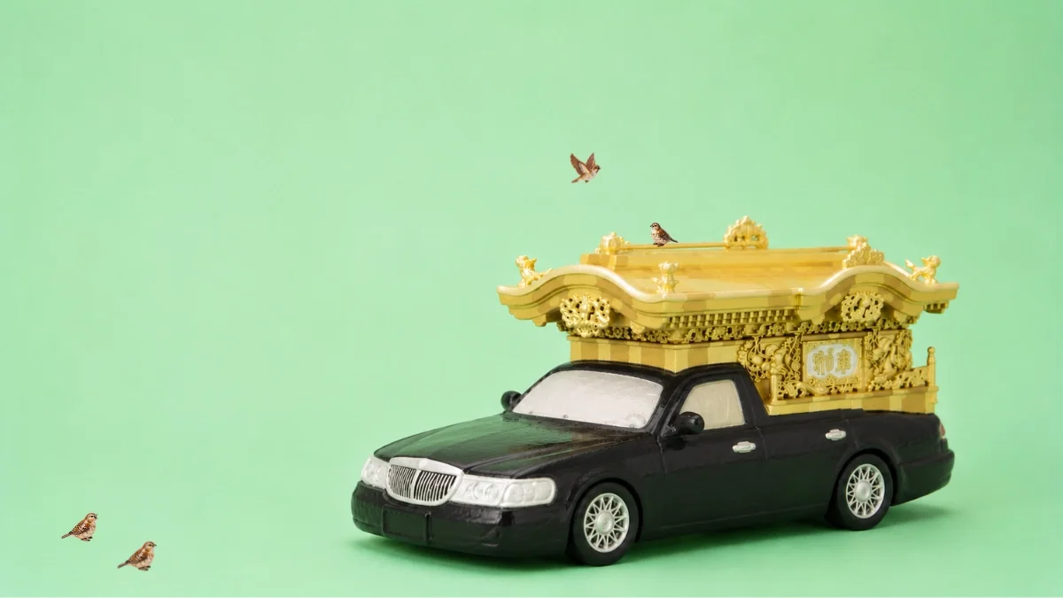 金色の宮型装飾を載せた宮型霊柩車のミニチュアと飛ぶ小鳥