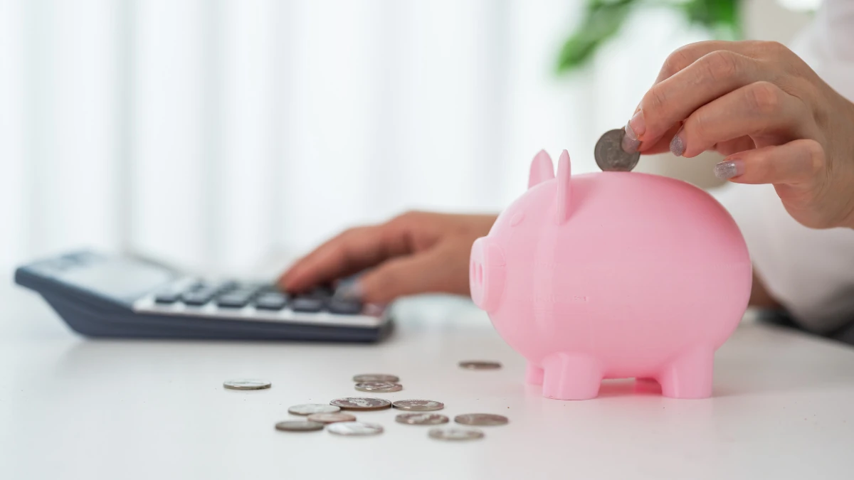 電卓を叩きながらピンクの貯金箱に硬貨を入れる手元、老後2000万円問題と資金準備を表す場面