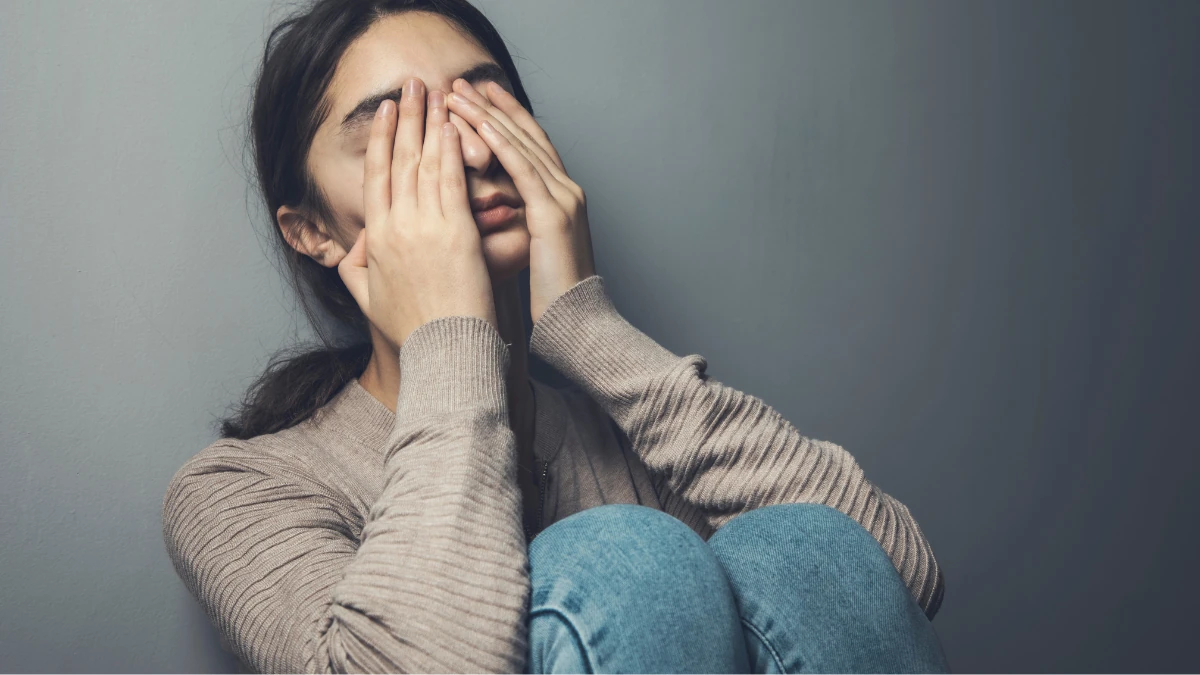 壁際で膝を抱え両手で顔を覆う女性、葬儀の後悔や不安に向き合う心情を表した場面