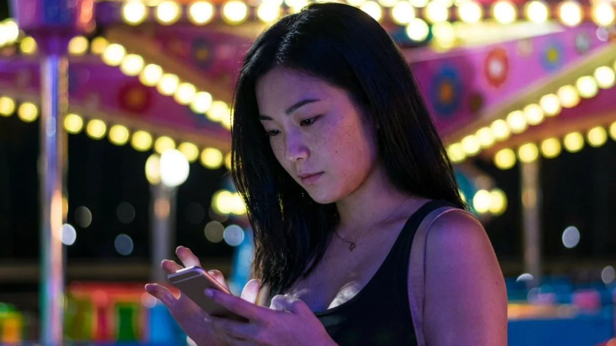 夜の遊園地でスマホを見つめ疲れた表情の女性で情報格差や疲弊を表す様子