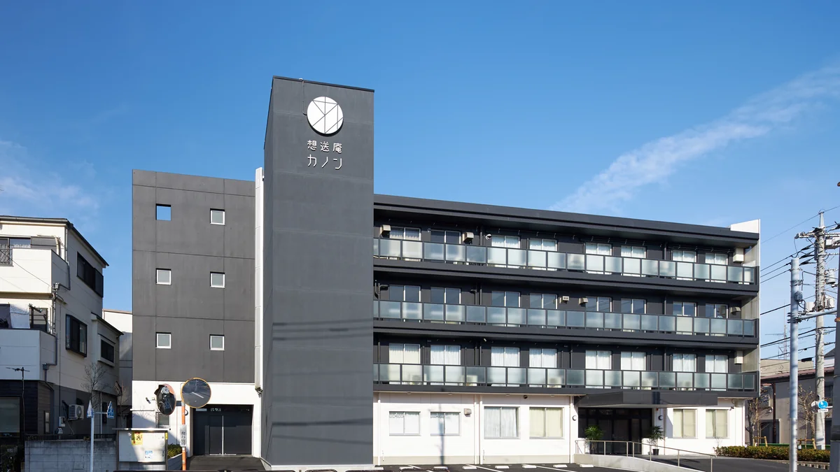 青空のもとに立つ想送庵カノンの外観。シンボルマークを掲げた時計塔が目印の4階建てで、葛飾区立石の住宅街に溶け込む落ち着いた佇まい
