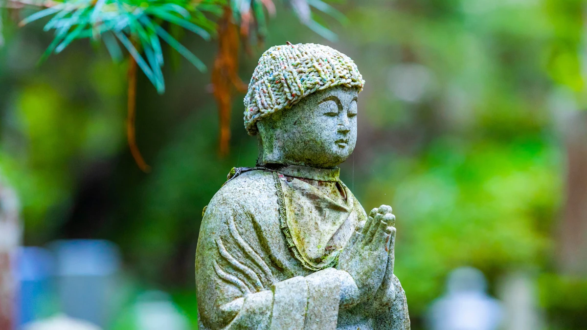 毛糸の帽子をかぶり墓地で静かに合掌する石のお地蔵さま。永代供養や合祀による故人の供養をイメージした情景