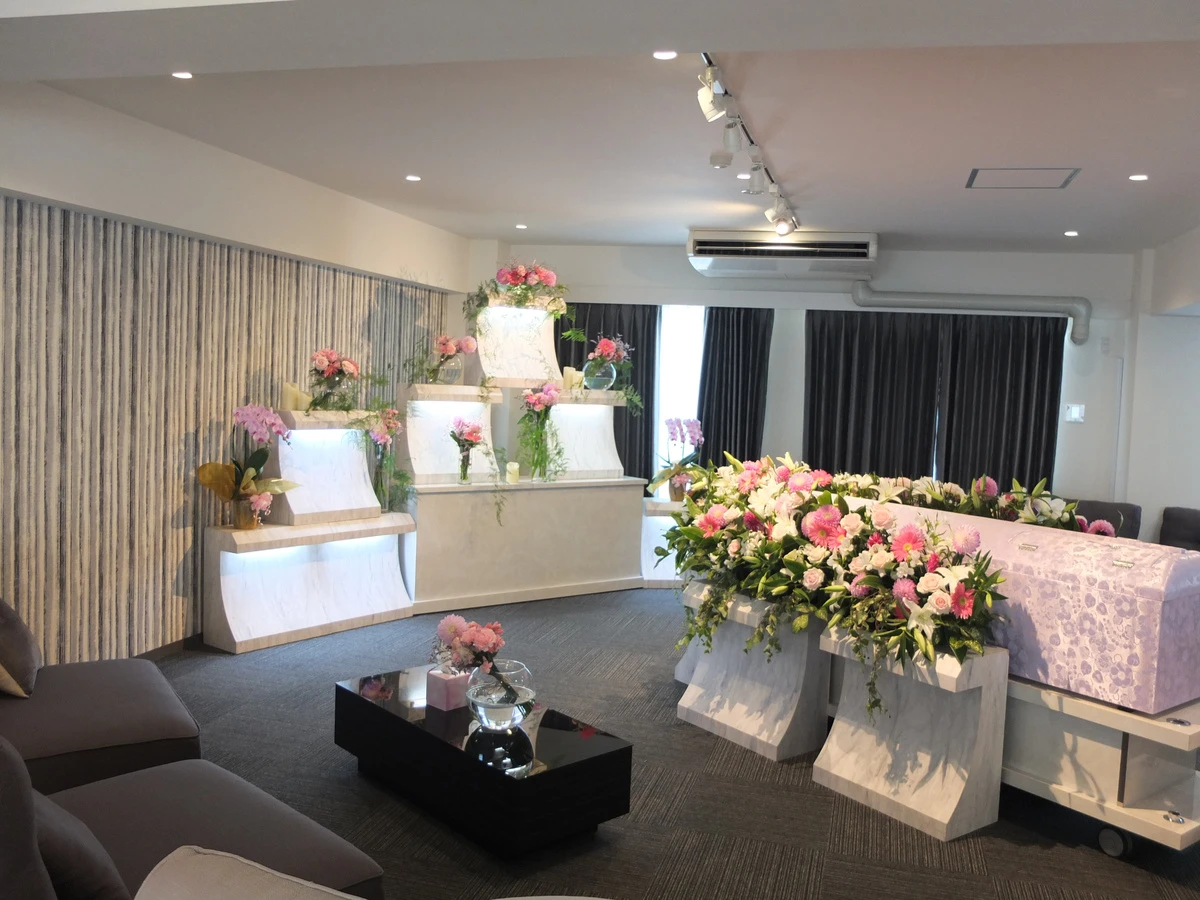 想送庵カノンの祭壇装飾事例、ピンクの百合とバラの供花が並ぶ白い祭壇。段違いの飾り台が柔らかな印象