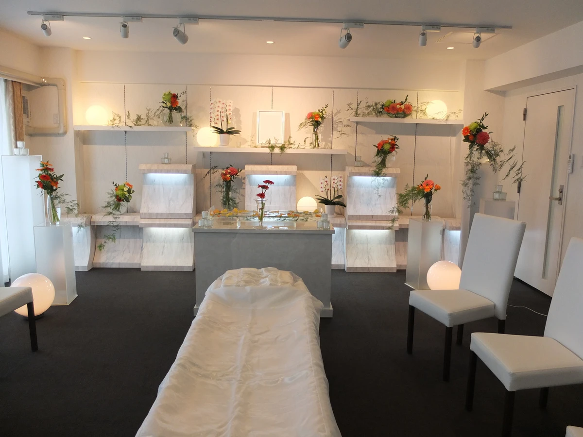 想送庵カノンの祭壇装飾事例、朱色とオレンジの花を大理石調の段飾りに。丸い照明が灯る明るい安置室