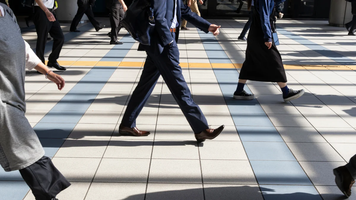 通勤時間帯の駅前を足早に歩く現役世代の人々の足元をとらえた写真