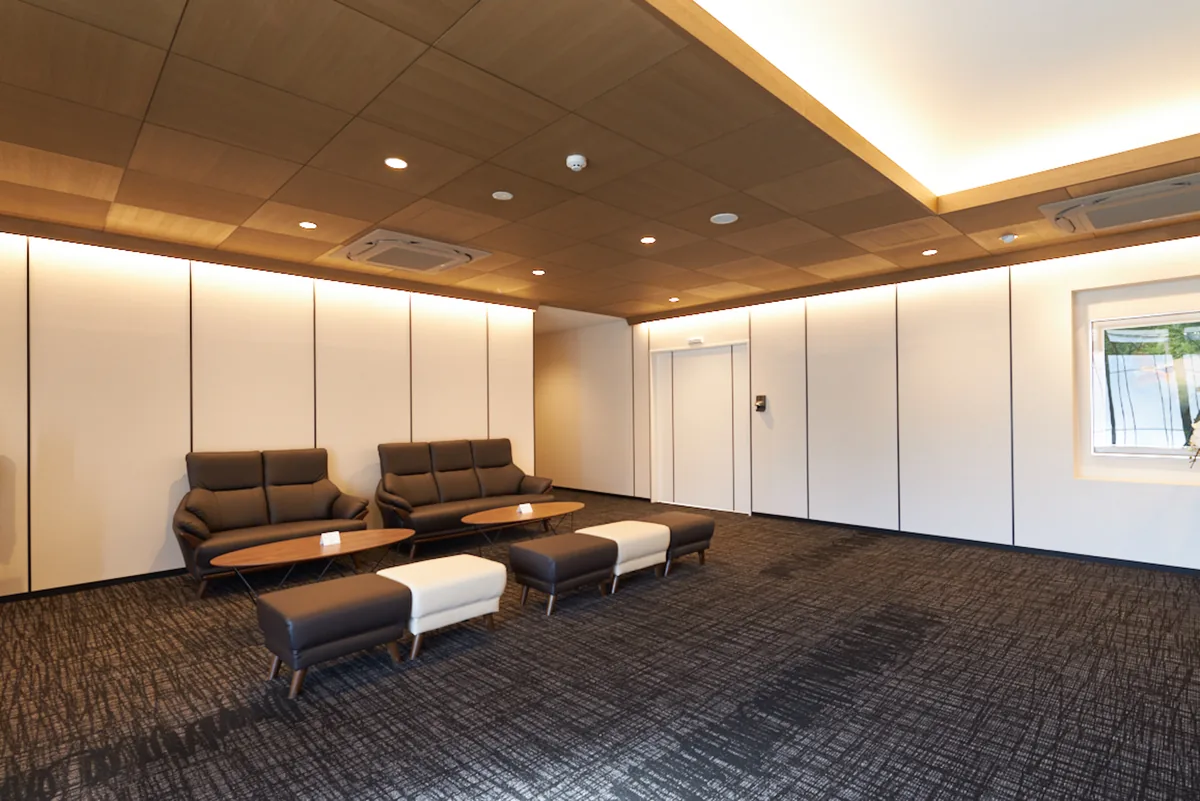 想送庵カノンのオープンラウンジ。木目の天井の下に革のソファー2脚とオットマンを置いた共用空間