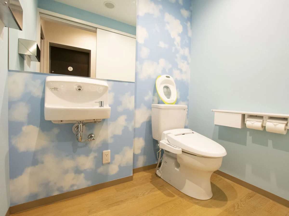 想送庵カノンのお子さま用トイレ。青空と雲の壁紙の個室に、子ども用の補助便座を置いた便器と小さな手洗いがある