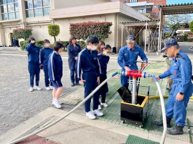 立石中学校の防災訓練で、消火栓に差し込んだスタンドパイプにホースをつなぎ、生徒たちに放水の手順を見せる消防団員