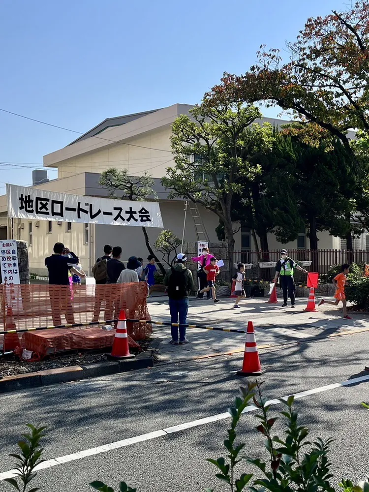第41回立石地区ロードレースの会場。「地区ロードレース大会」の横断幕とコーンが並ぶコースを子どもたちが走っている