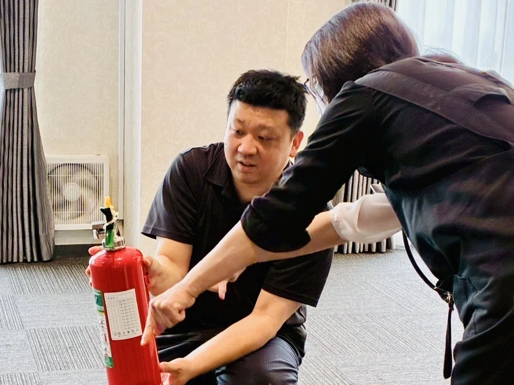 想送庵カノンの館内の防災訓練で、消防団員のスタッフが消火器を手に、ほかのスタッフに使い方を教えている