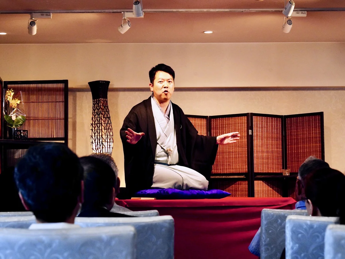 第4回「ご供養落語」の高座で、両手を広げて噺を演じる三遊亭仁馬さんと、聞き入る客席