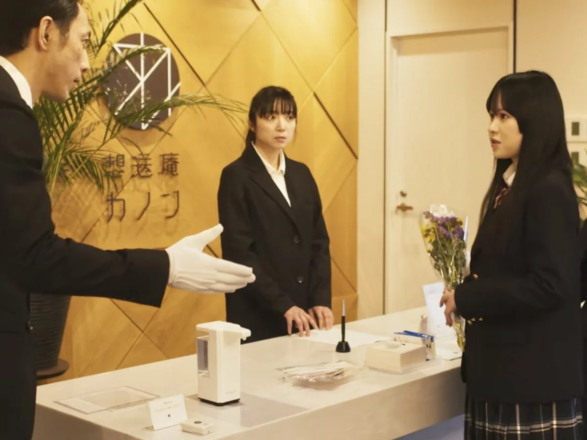 啓発動画「絶対零度のオアシス」エピソード3の告別式の場面。「想送庵 カノン」のロゴがある受付で、白手袋の男性が花束を持つ制服姿の女性を案内している
